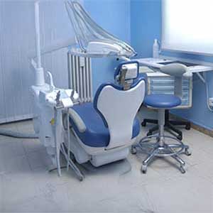 An image depicting a dental office setup, featuring a dental chair with footrests, an examination table, and various dental equipment.