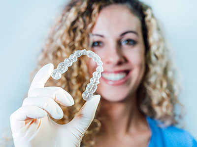 A woman is holding a clear plastic dental retainer.