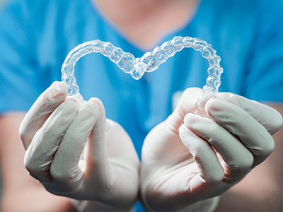 A healthcare worker s hand holding a transparent heart-shaped dental appliance, symbolizing care and compassion in the dental field.