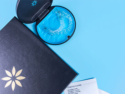 A blue and black toothbrush with a clear bristle head, placed on top of an open package that reads  Crystals  in gold lettering.