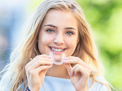 A young woman with a radiant smile, holding up her clear orthodontic aligners.