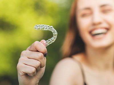 An image of a smiling woman holding up a clear plastic toothbrush with bristles.