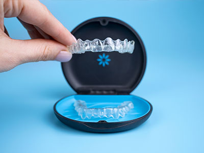 A hand holding a clear dental impression tray with a blue lid, revealing the impression of a set of teeth inside.