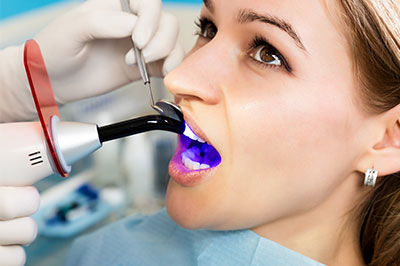 A woman receiving a dental cleaning with a device that sprays water and possibly cleansing solution, while seated in a dentist s chair.