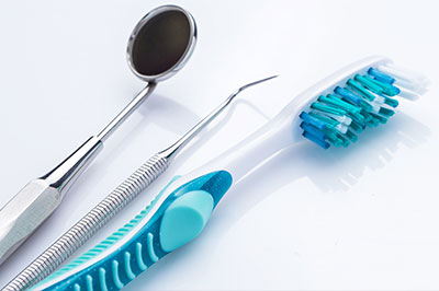 The image displays a collection of dental care tools, including a toothbrush with blue bristles and a pair of scissors-like instruments, against a white background.