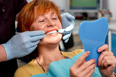 A woman in a dental chair receiving dental care, with a dental professional adjusting her mouthpiece.