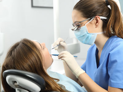 A dental hygienist is performing a cleaning procedure on a patient s teeth, with the patient seated in the dental chair and wearing protective eyewear.