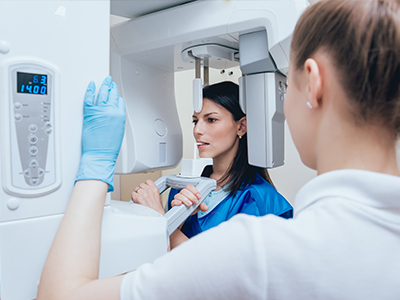 Two individuals in a medical setting, with one person operating a large, modern scanner and the other wearing protective gloves and standing beside it.