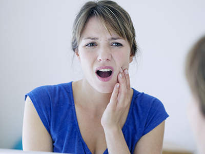 The image shows a woman with her mouth open, displaying concern or surprise, looking at her reflection in the mirror.