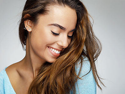 A woman with long hair smiles at the camera, showcasing a close-up of her face against a neutral background.