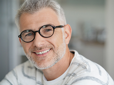 The image shows a middle-aged man with short gray hair, wearing glasses and a white shirt, smiling at the camera.