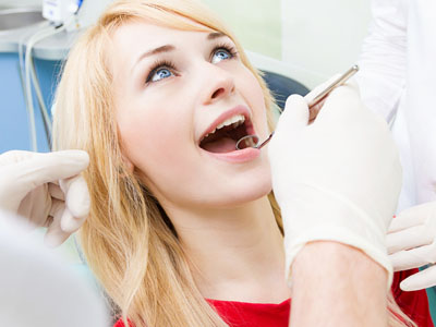 A woman sitting in a dental chair while receiving dental care, with a dentist performing the procedure.