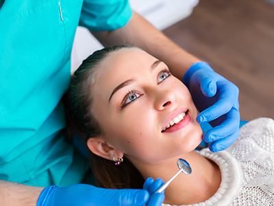 A dental professional performing a procedure on a patient s teeth while the patient smiles and looks content.