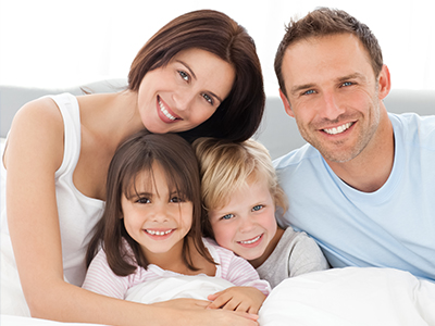 A family of four, including an adult couple and two children, poses for a photograph with smiles on their faces.