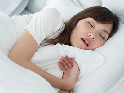 A woman is peacefully sleeping in a bed with her eyes closed, and she appears to be resting her head on a pillow.