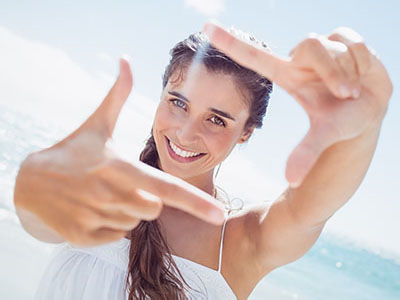 A smiling woman taking a selfie with her hand in front of her face.