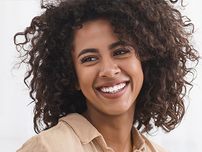 The image is a portrait of a smiling woman with curly hair, wearing a beige top and looking directly at the camera.